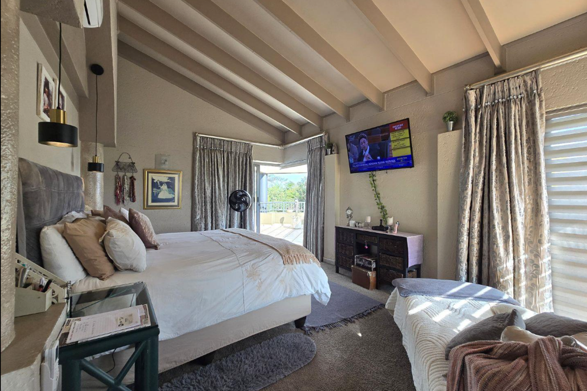 Spacious bedroom featuring high exposed beam ceilings, carpeted flooring, and direct access to an outdoor balcony through sliding glass doors.