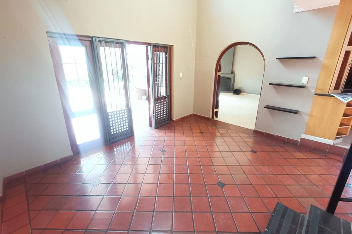 Spacious living area featuring terracotta floor tiles, an arched doorway, built-in wall shelving, and double doors providing direct access to the outdoor patio.