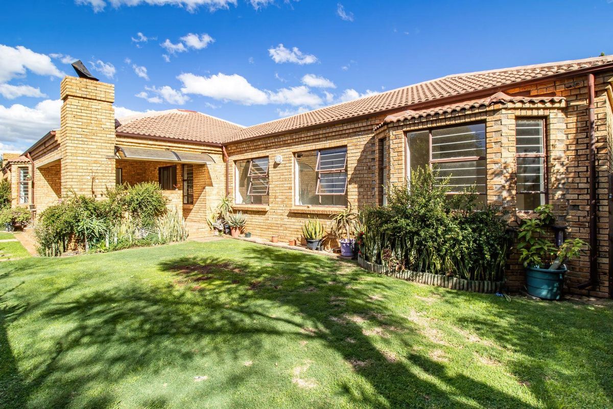 Rear view of a face-brick cluster home featuring a tiled roof, chimney, and established garden area.
