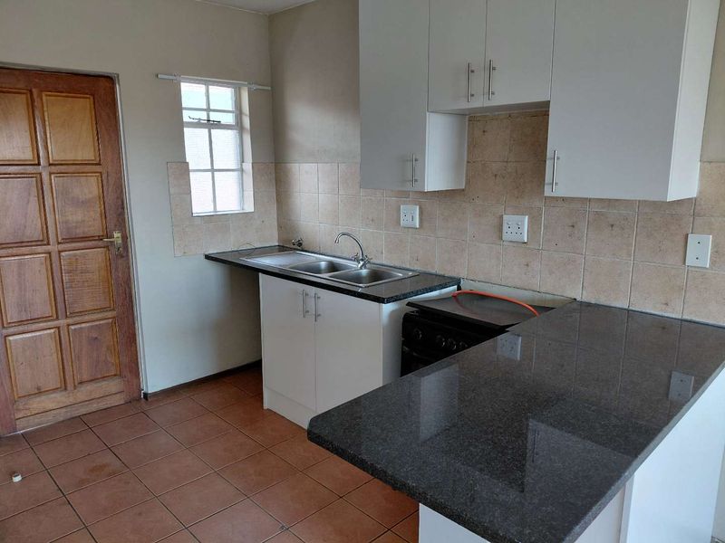 A functional kitchen featuring white cabinetry, dark granite countertops, a double basin sink, and tiled flooring, offering a clean and practical workspace.