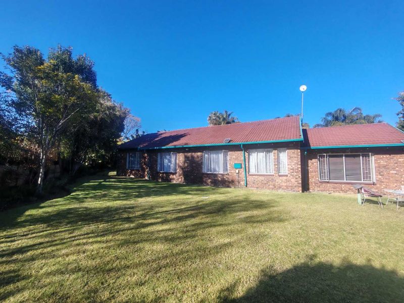 A rear view of a single-story brick house featuring a tiled roof and a spacious lawn area.