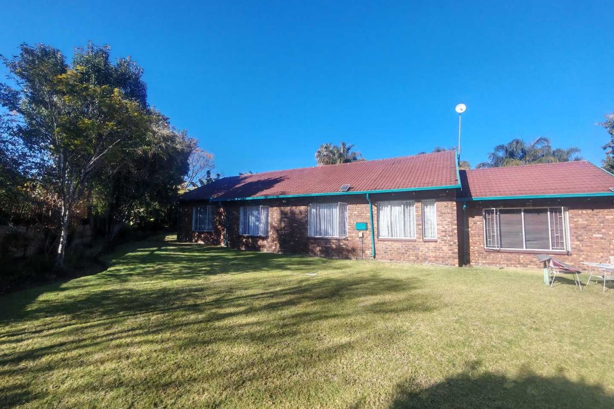 A rear view of a single-story brick house featuring a tiled roof and a spacious lawn area.