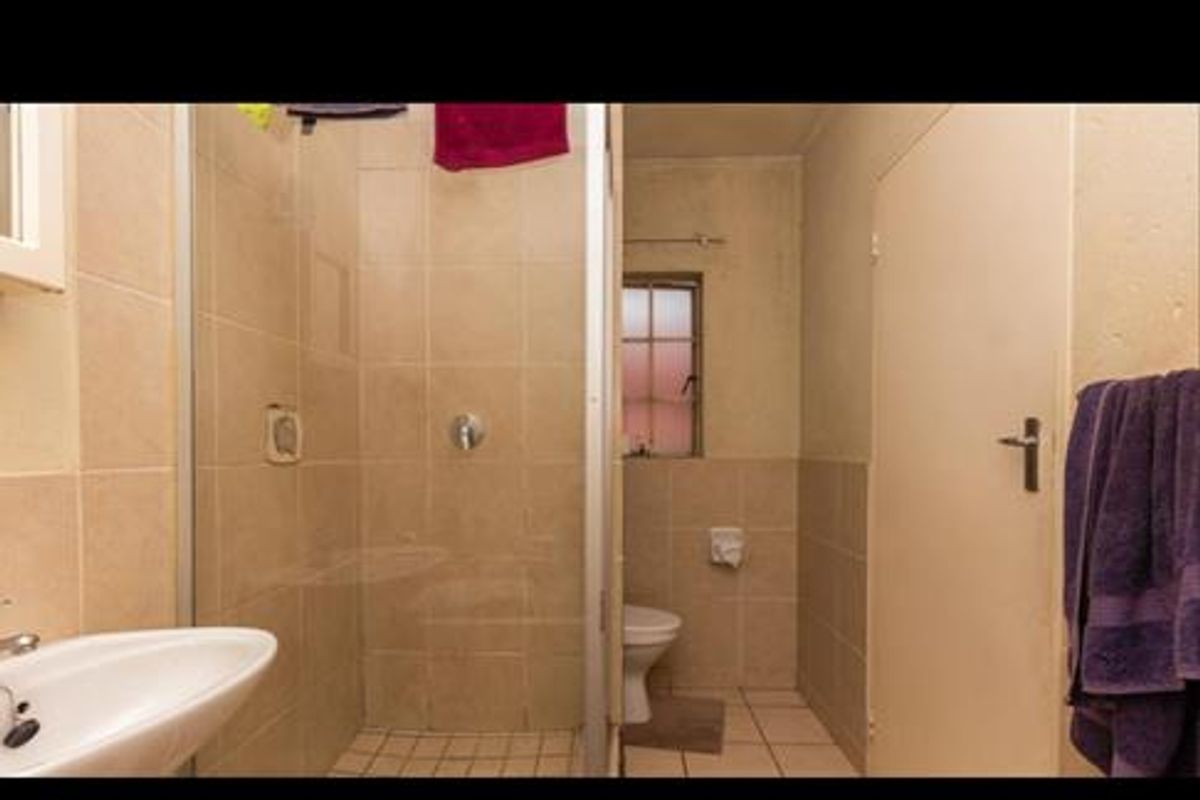 A dated bathroom featuring a glass-enclosed shower, pedestal sink, and toilet with neutral wall and floor tiling.