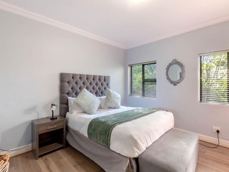 A well-maintained bedroom featuring light-toned laminate flooring, coving, and dual windows fitted with venetian blinds.