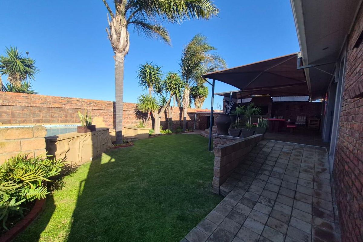 Rear garden area featuring a swimming pool, paved walkway, and a covered patio with a built-in braai, enclosed by brick boundary walls.