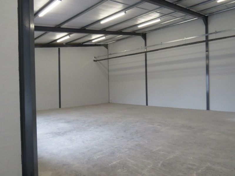 A clean, open-plan industrial warehouse space featuring exposed steel structural beams, polished concrete flooring, and high-mounted fluorescent lighting.