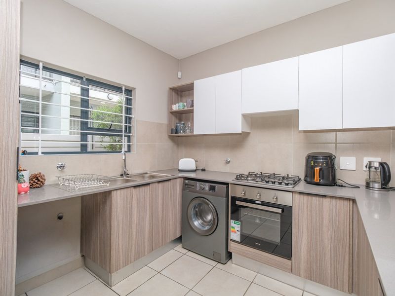 Modern kitchen featuring wood-grain cabinetry, stone countertops, gas hob, built-in oven, and tiled flooring with a window overlooking the exterior.