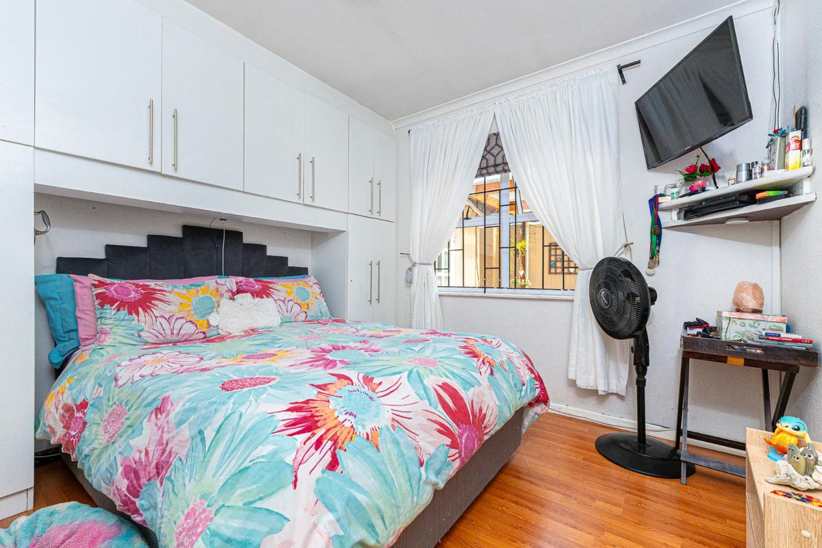 A bedroom featuring built-in overhead cabinetry, laminate flooring, and a window with security bars.