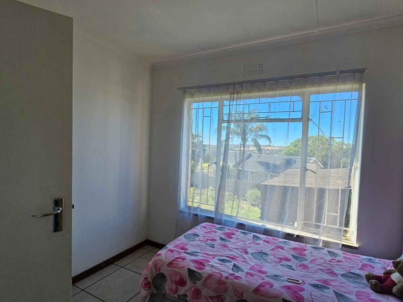 A functional bedroom featuring tiled flooring and a large window with security bars, offering natural light and a view of the surrounding area.