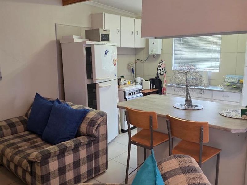 Open-plan living and kitchen area featuring tiled flooring, a breakfast bar, and functional kitchen cabinetry with a gas stove and geyser.