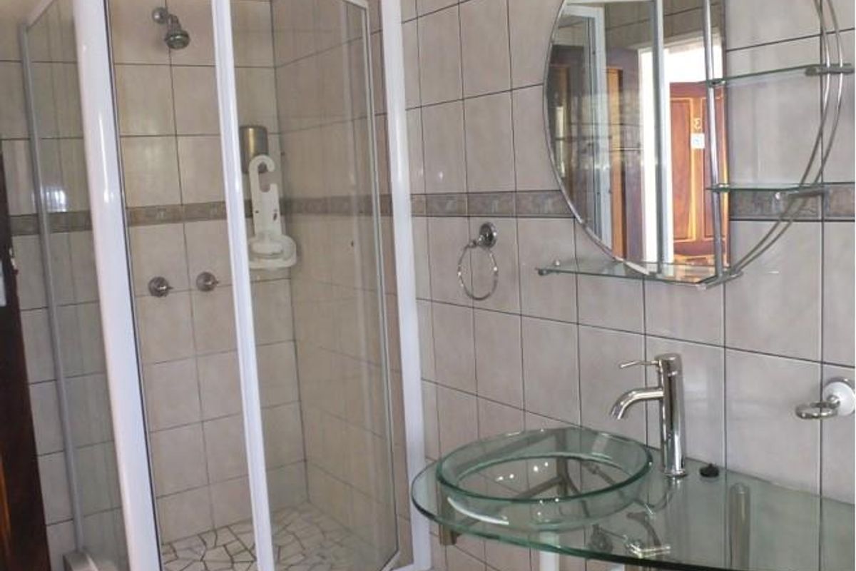 A functional bathroom featuring a glass vessel sink, a corner shower enclosure with tiled walls, and a circular wall-mounted mirror.