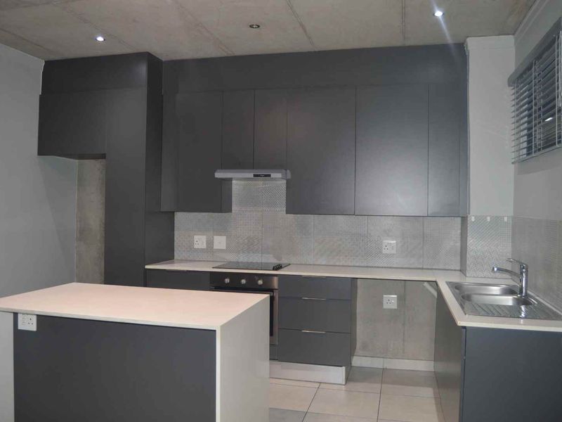 Modern kitchen featuring dark grey cabinetry, stone countertops, a central island, and integrated stainless steel appliances, offering a clean and functional cooking space.