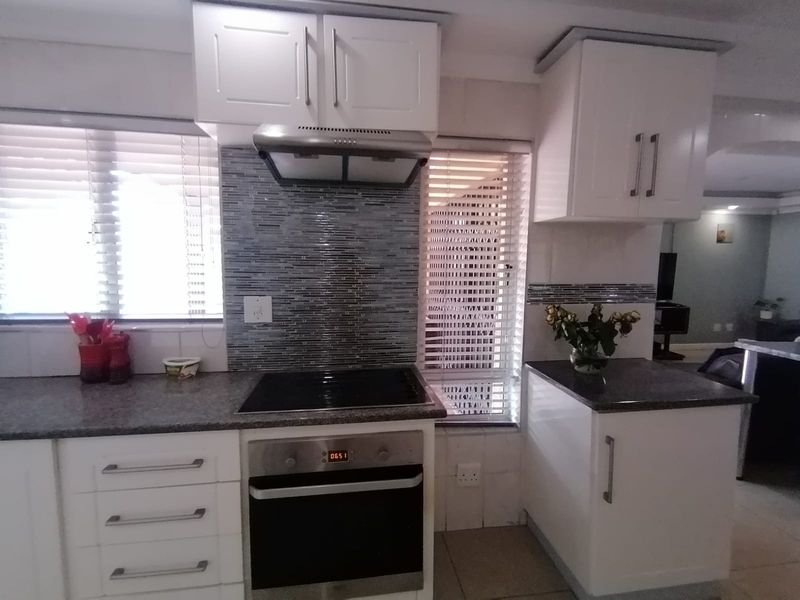 A functional kitchen featuring white cabinetry, stone countertops, a mosaic tile backsplash, and integrated stainless steel appliances including an oven and hob.