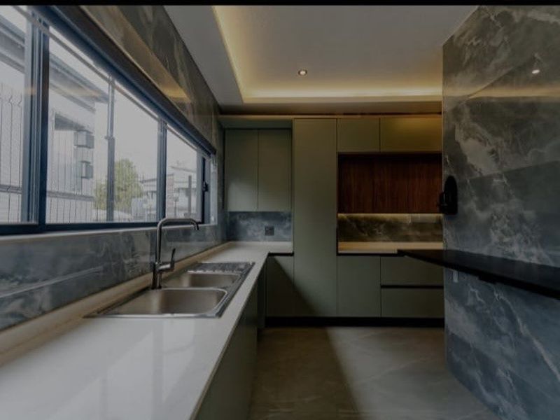 Modern kitchen featuring sleek green cabinetry, stone countertops, double bowl sink, and elegant marble-effect wall tiling with integrated recessed lighting.