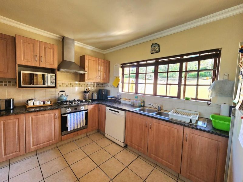 A functional kitchen featuring wooden cabinetry, granite countertops, a gas hob, stainless steel extractor fan, and tiled flooring with ample natural light.