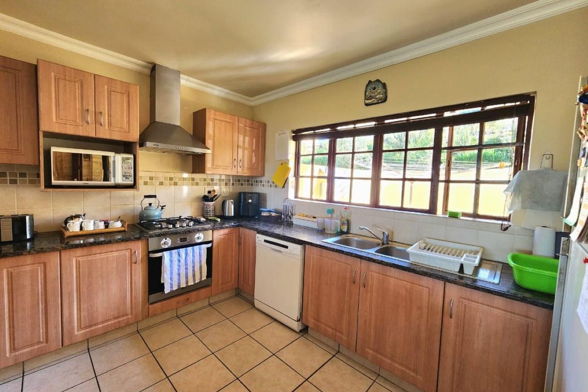 A functional kitchen featuring wooden cabinetry, granite countertops, a gas hob, stainless steel extractor fan, and tiled flooring with ample natural light.