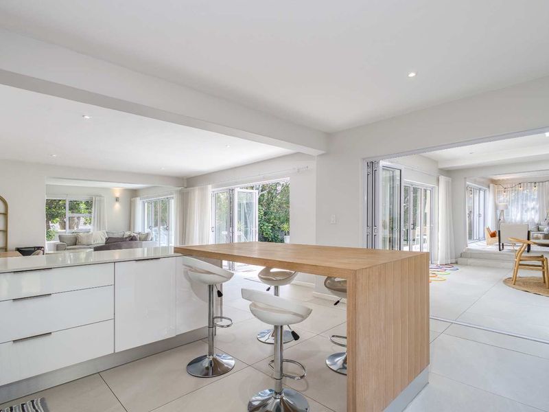 Bright open-plan living area featuring a modern kitchen island with timber breakfast bar, sleek white cabinetry, and seamless access to outdoor spaces via bi-fold doors.