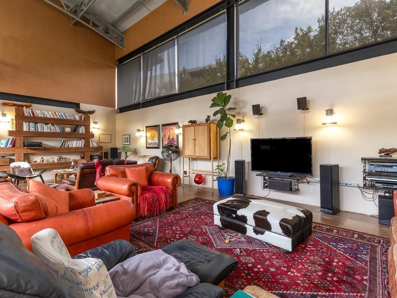 Spacious living room featuring high vaulted ceilings with exposed steel trusses, large clerestory windows for natural light, and custom built-in wooden shelving.