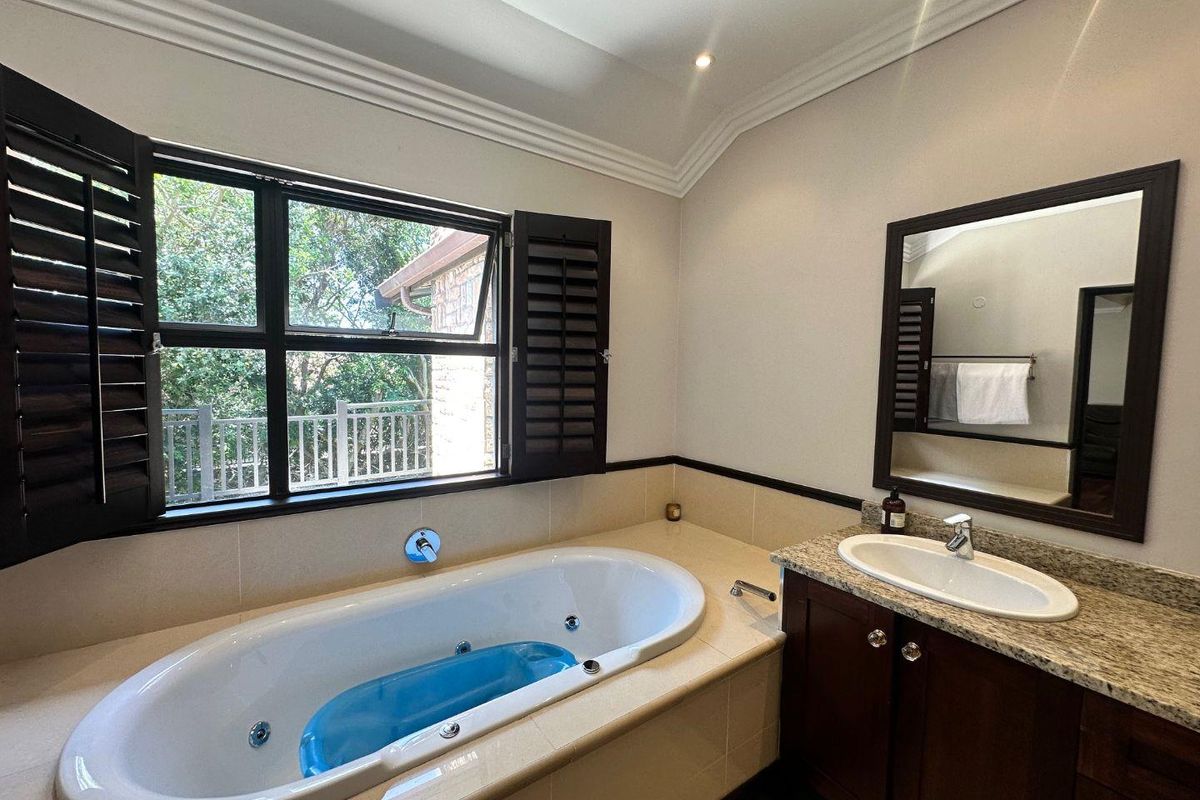 A well-maintained bathroom featuring a built-in jetted bathtub, granite-topped vanity with integrated sink, and dark wood plantation shutters.