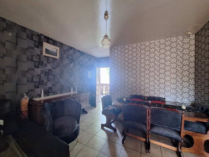 A dining and living area featuring patterned wallpaper, tiled flooring, and a central pendant light fixture with access to an outdoor balcony.