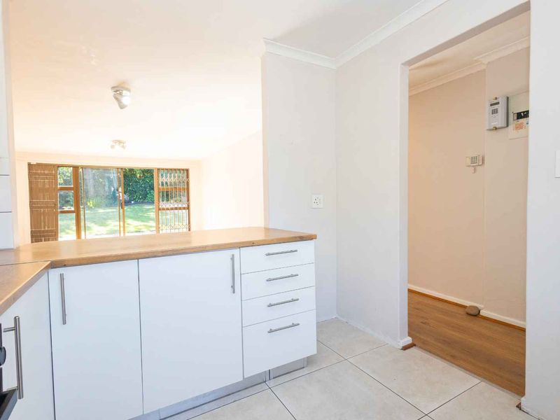 A bright, modern kitchen featuring white cabinetry, wooden countertops, and tiled flooring, with an open-plan layout leading to a garden-facing living area.