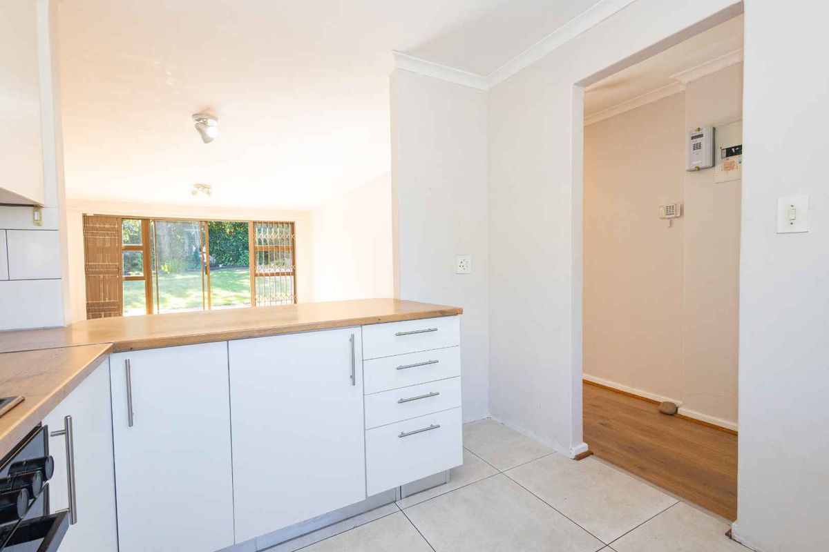 A bright, modern kitchen featuring white cabinetry, wooden countertops, and tiled flooring, with an open-plan layout leading to a garden-facing living area.