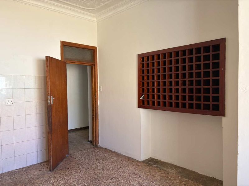 An empty kitchen area featuring a built-in wooden wine rack, tiled splashback, and classic ornate ceiling cornicing, awaiting renovation or modernization.