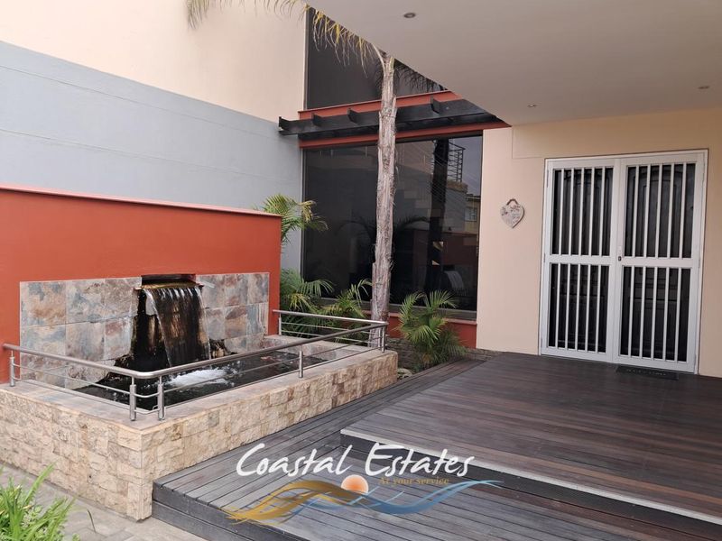 A well-maintained outdoor patio area featuring timber decking, a built-in stone water feature, and secure access to the interior.