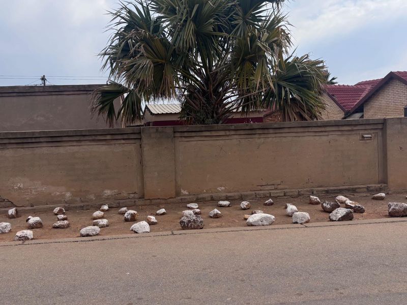 Street view of the property showing a perimeter wall, metal gate, and solar water heater installation on the roof.