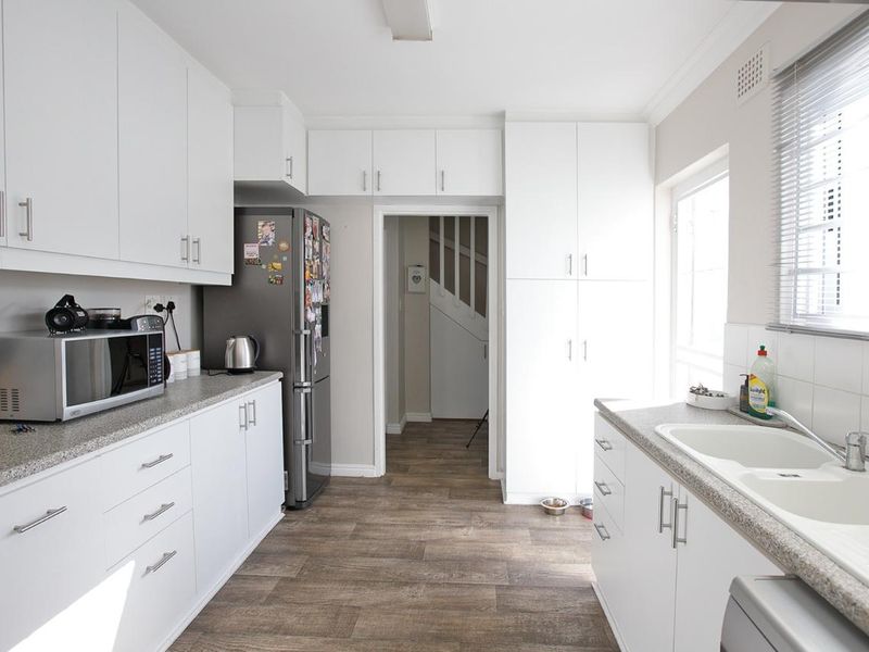 A clean, functional kitchen featuring white cabinetry, durable laminate countertops, a double basin sink, and wood-look vinyl flooring with ample storage space.