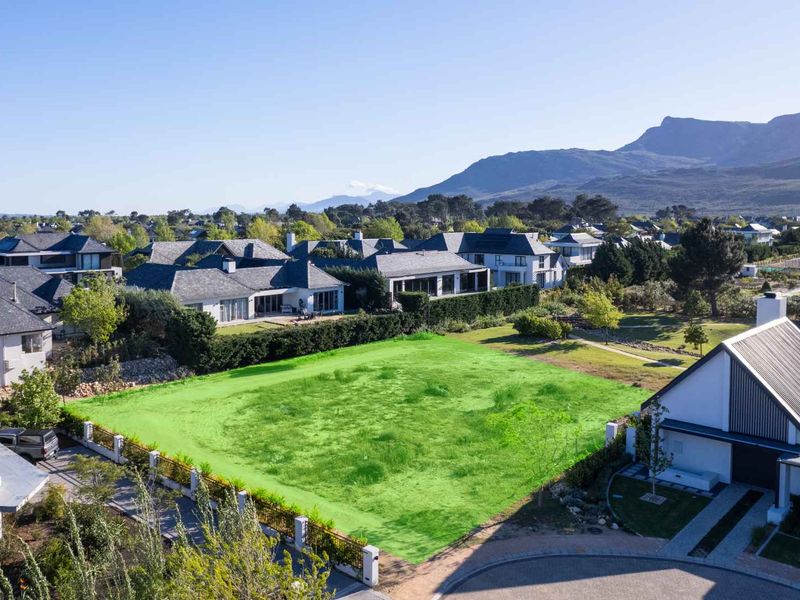 An aerial view of a vacant residential plot in a developed estate, featuring established landscaping and surrounding luxury homes with mountain views.