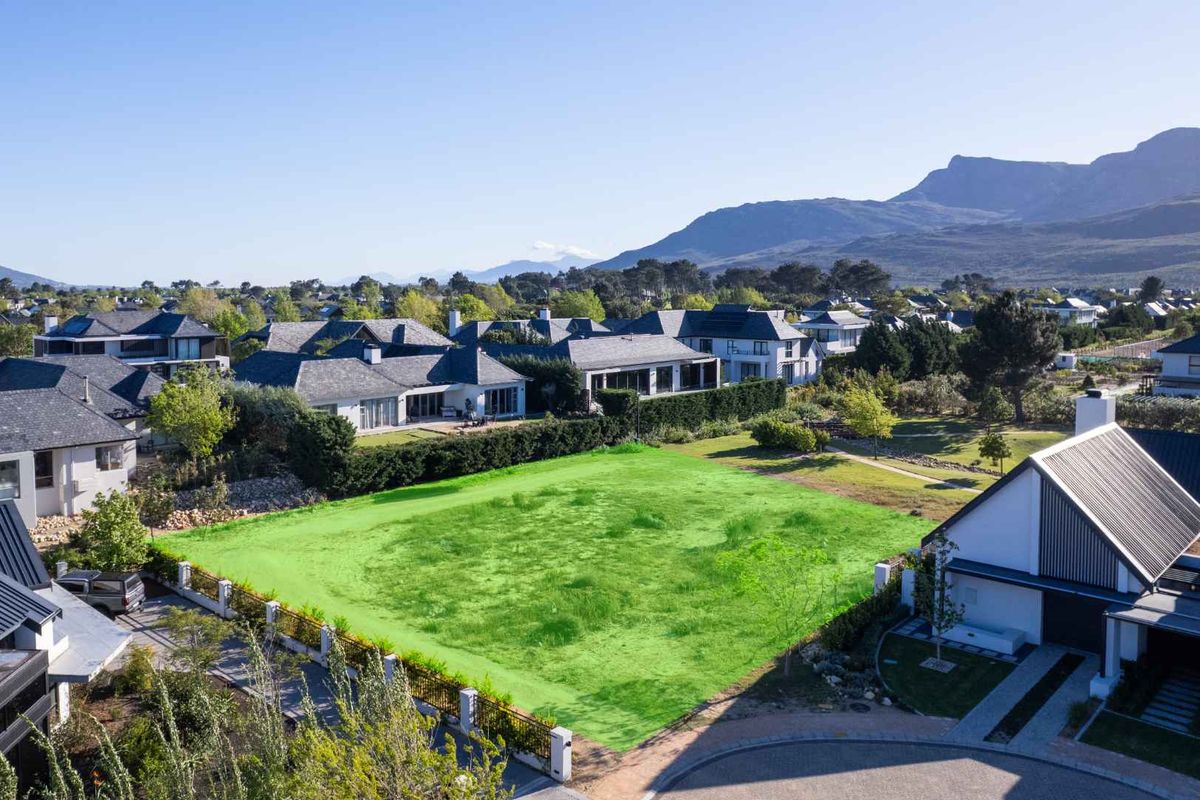 An aerial view of a vacant residential plot in a developed estate, featuring established landscaping and surrounding luxury homes with mountain views.