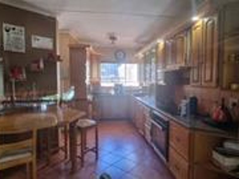 A functional kitchen featuring wooden cabinetry, built-in oven and hob, and tiled flooring, offering a traditional layout with ample storage space.