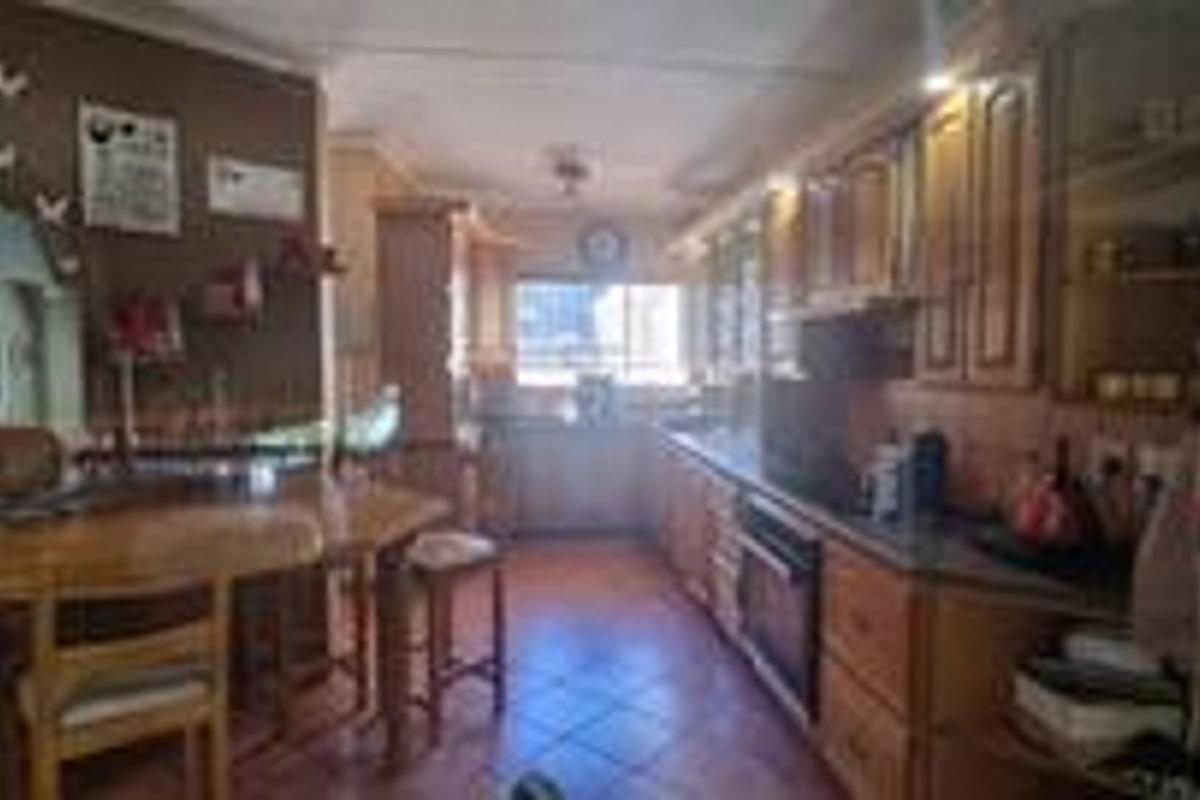 A functional kitchen featuring wooden cabinetry, built-in oven and hob, and tiled flooring, offering a traditional layout with ample storage space.