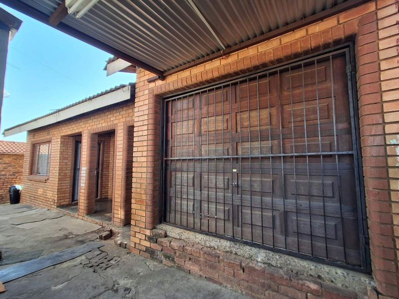 Exterior view of a face brick house featuring a wooden garage door with security gate and a corrugated metal roof covering the entrance area.