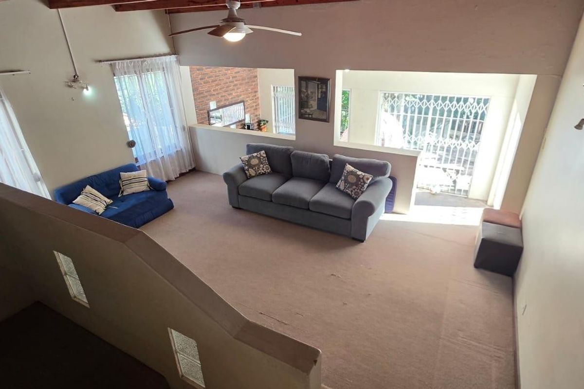 Spacious living area featuring exposed timber ceiling beams, a ceiling fan, and large windows with security gates, offering a bright and open atmosphere.