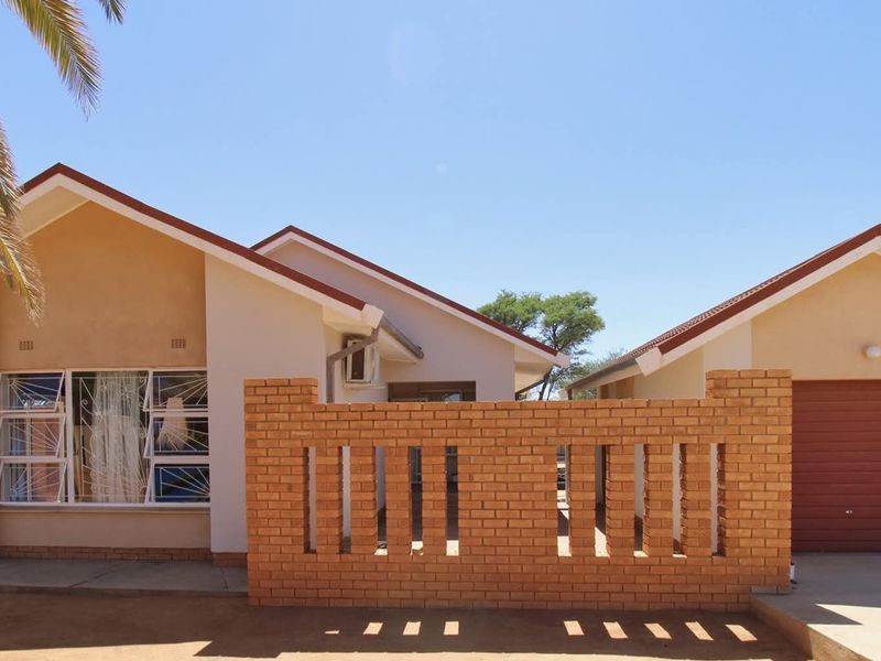 Front elevation of a single-story house featuring a brick boundary wall, tiled roof, and an integrated garage with a roller door.