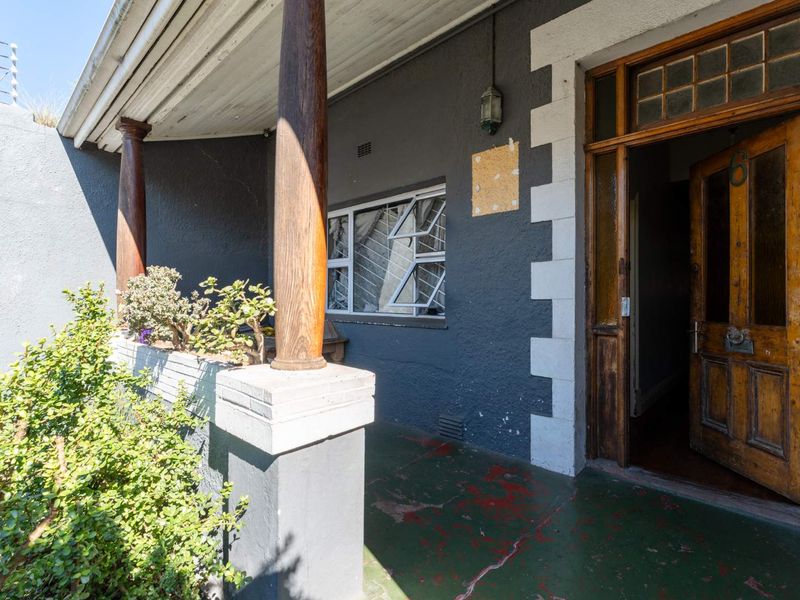 Covered front porch featuring wooden support columns, a classic timber entrance door, and a painted concrete floor in need of maintenance.