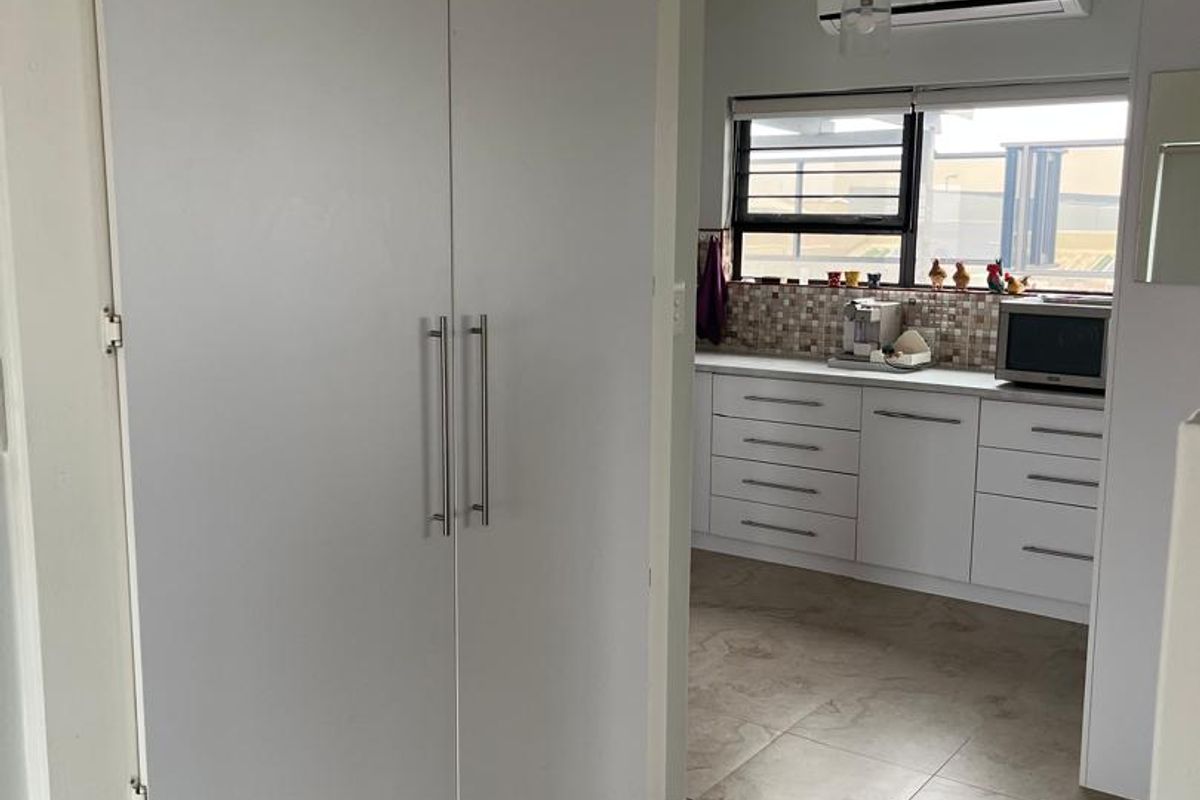 A functional kitchen area featuring white cabinetry, tiled flooring, a mosaic backsplash, and a wall-mounted air conditioning unit.