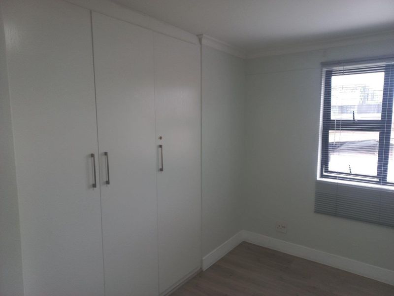 A clean, empty bedroom featuring neutral walls, laminate flooring, and white built-in cupboards with modern handles.