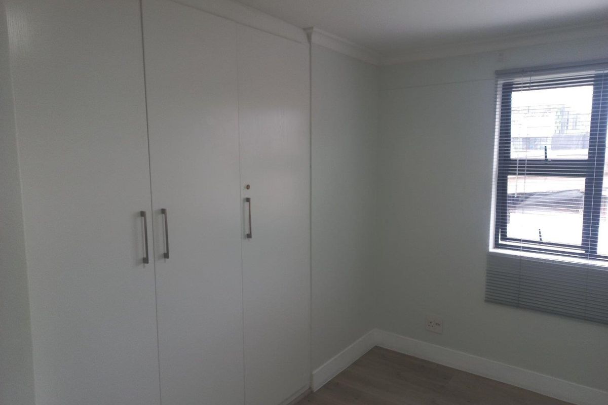 A clean, empty bedroom featuring neutral walls, laminate flooring, and white built-in cupboards with modern handles.