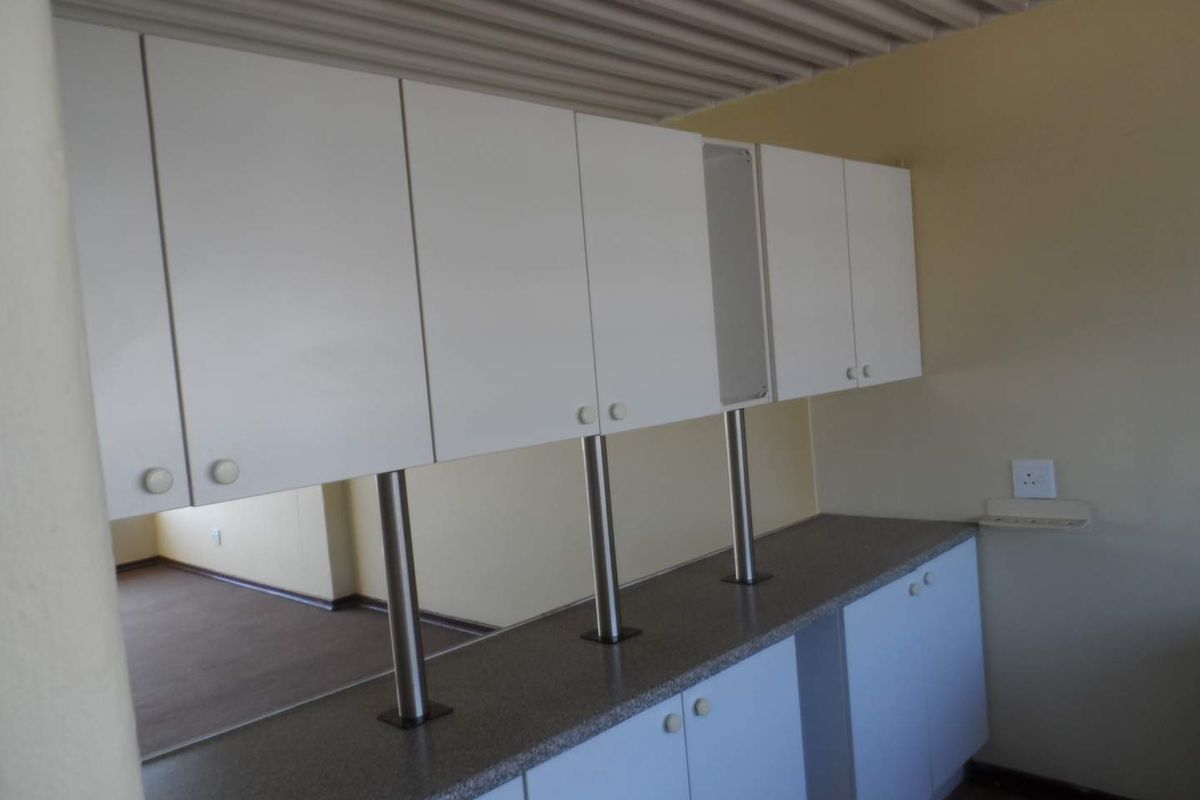 A functional kitchen area featuring white cabinetry, stone-look countertops, and stainless steel support pillars, providing ample storage and workspace.