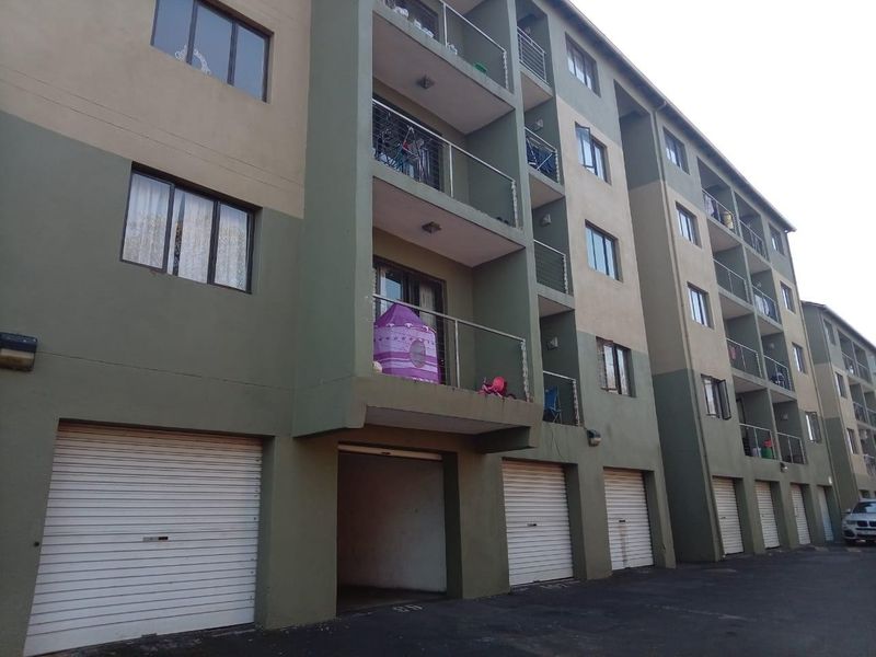 Exterior view of a multi-story apartment complex featuring ground-level roller garage doors and upper-level balconies with metal railings.
