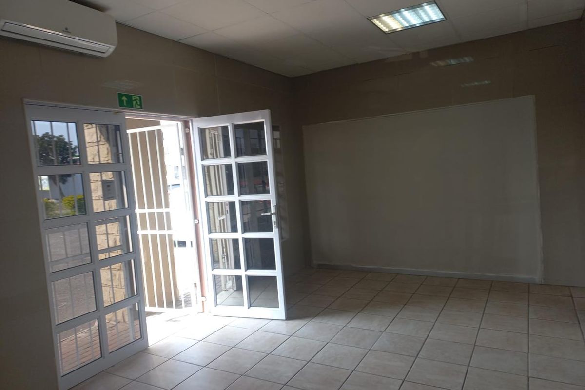 An empty office space featuring tiled flooring, recessed lighting, a split-system air conditioner, and glass panelled double doors with an external security gate.
