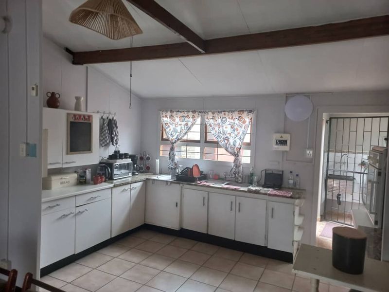 A functional kitchen featuring white cabinetry, laminate countertops, double sink, and exposed timber ceiling beams, with tiled flooring throughout.