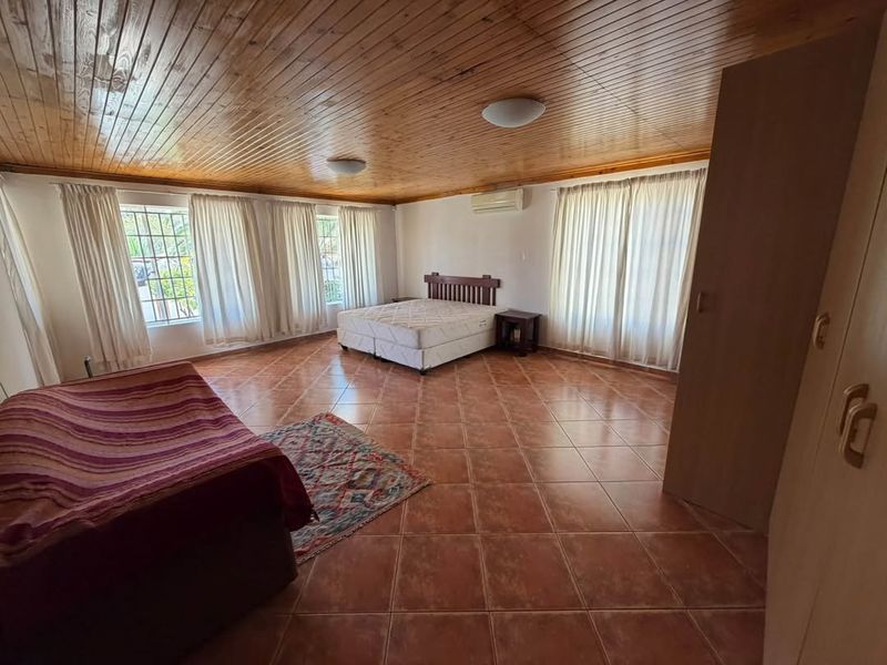 Spacious bedroom featuring a warm timber-clad ceiling, tiled flooring, built-in cupboards, and a split-system air conditioner for climate control.