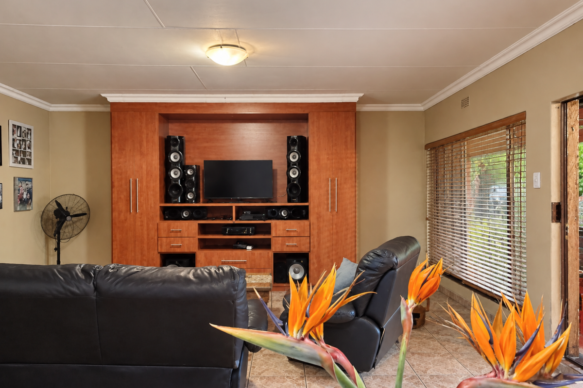 A living room featuring built-in wooden cabinetry, tiled flooring, and natural light through venetian blinds, offering a functional space for entertainment.