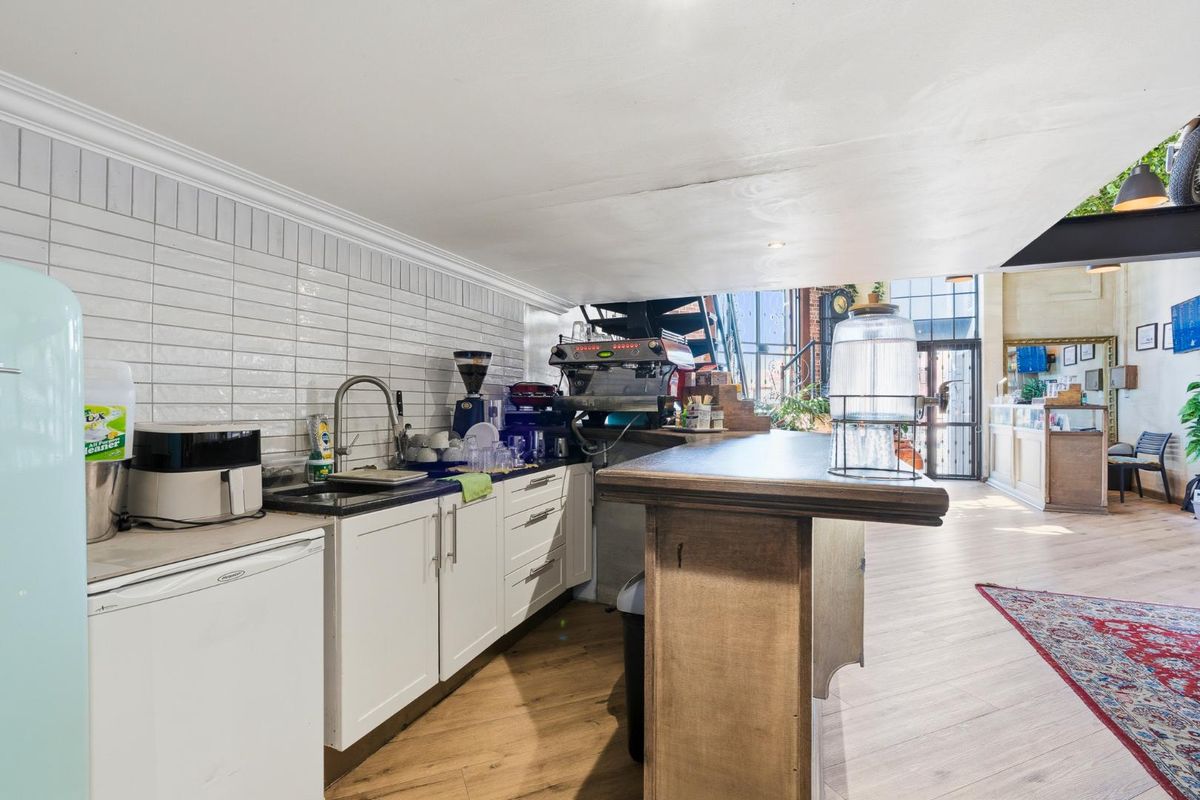 A functional kitchen area featuring white cabinetry, subway tile backsplash, a dark countertop, and a wooden service counter in an open-plan retail space.