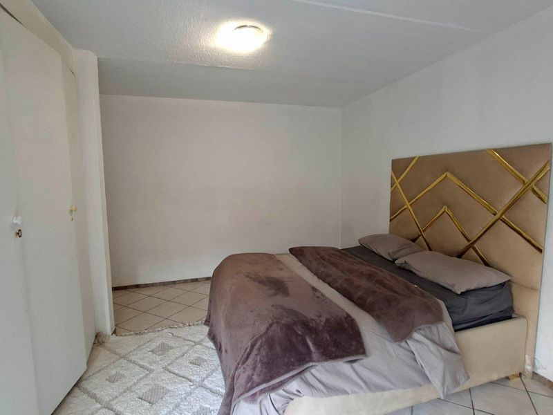 A bedroom featuring tiled flooring, a built-in wardrobe, and a ceiling light fixture, offering a functional space ready for personalization.
