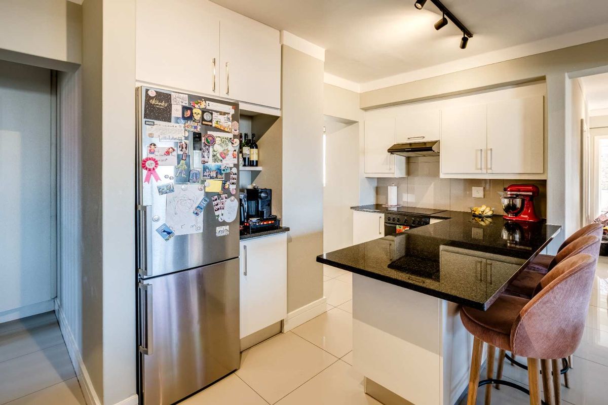 Modern kitchen featuring white cabinetry, black granite countertops, a breakfast bar, and integrated extractor fan, finished with neutral floor tiles.